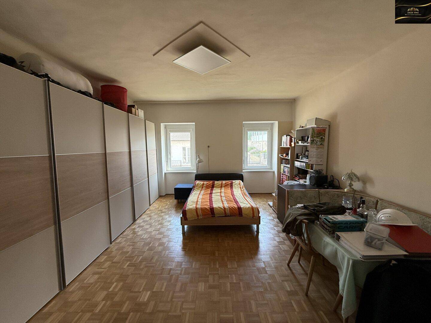 Geräumiges Schlafzimmer mit Parkettboden, großen Schränken und zwei Fenstern.