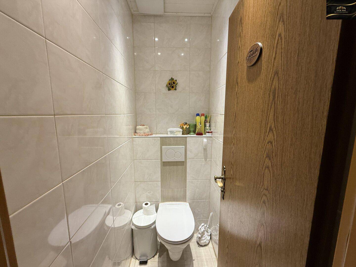 Kleines WC mit Wand-WC, Waschbecken und hellen Fliesen an Wänden und Boden.