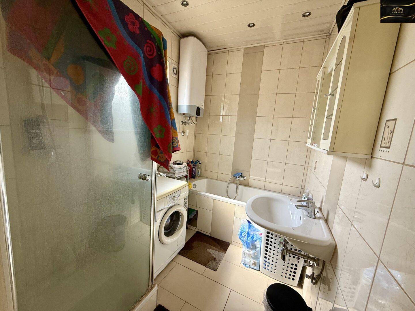 Badezimmer mit Dusche, Badewanne, Waschbecken und hellen Fliesen an Wänden und Boden.