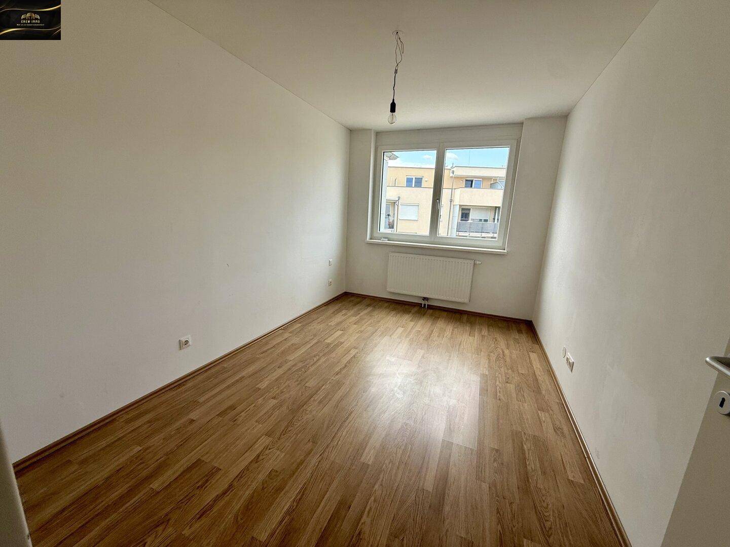 Geräumiges Schlafzimmer mit hellem Laminatboden und einem Fenster mit Blick auf die Umgebung.