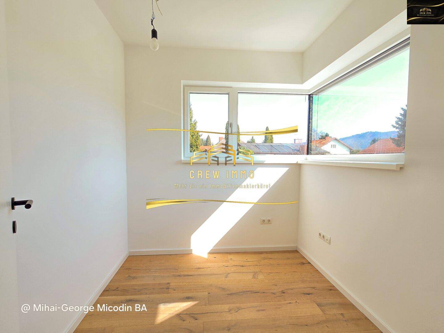 Helles Zimmer mit Holzparkett und großem Fenster, das viel Tageslicht hereinlässt.
