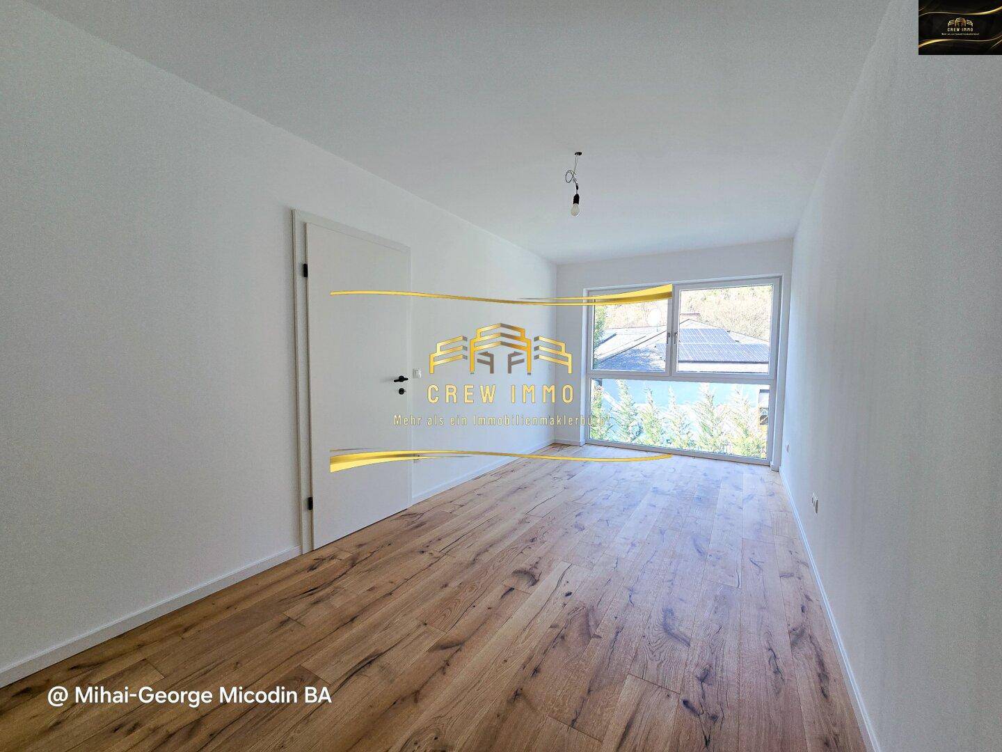 Helles Zimmer mit Holzparkett und großem Fenster, das Zugang zu einem Außenbereich bietet.