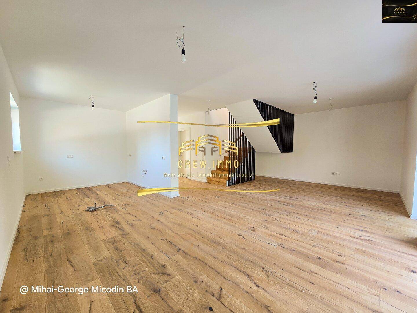Geräumiger, heller Wohnbereich mit elegantem Holzparkett und moderner Treppe, bereit zur Einrichtung.