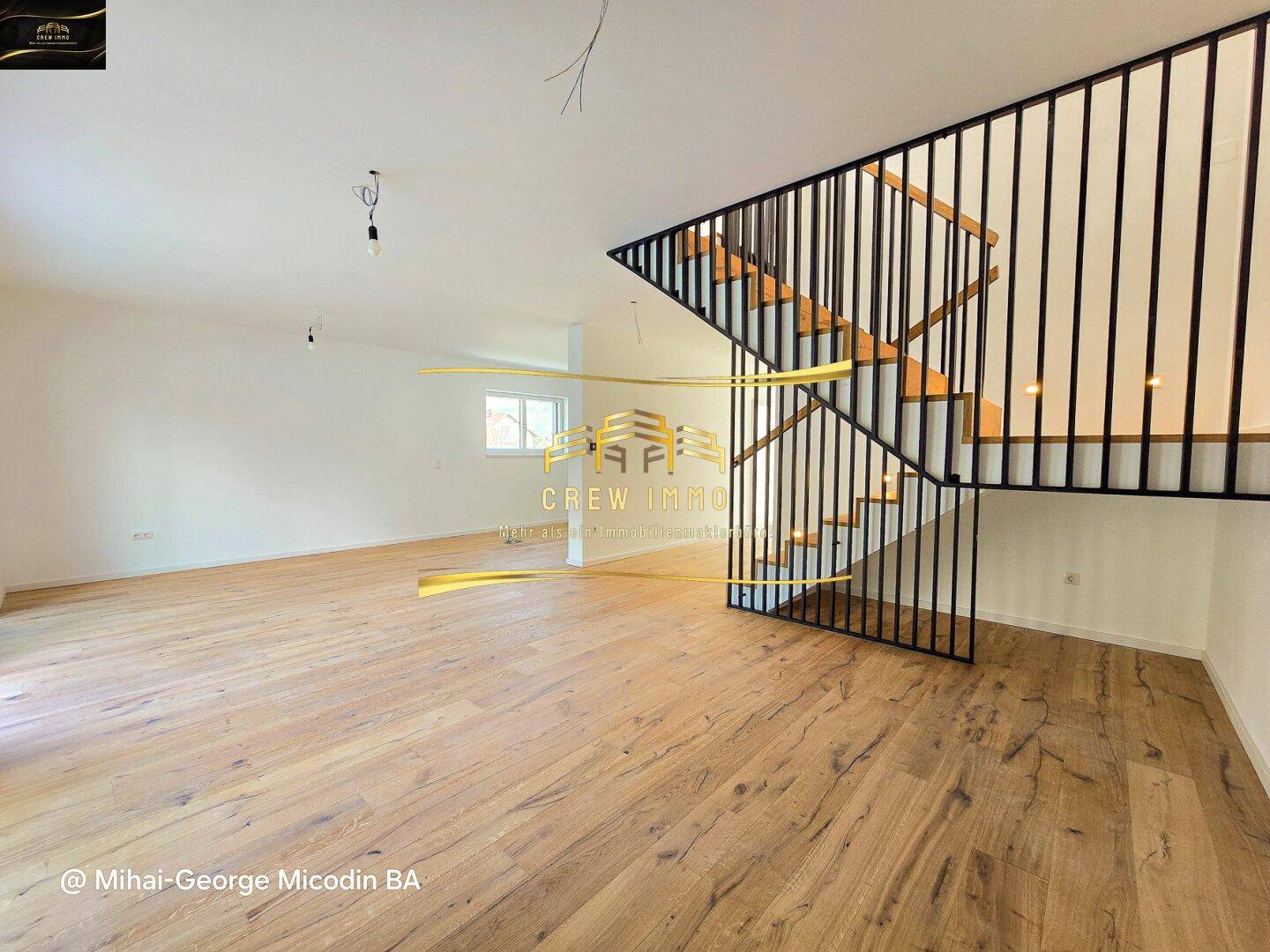 Heller Wohnbereich mit Holzboden und moderner Treppe mit schwarzem Geländer.