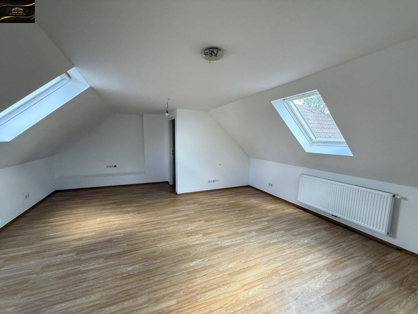 Heller Dachbodenraum mit Laminatboden und zwei Dachfenstern, die für viel Licht sorgen.