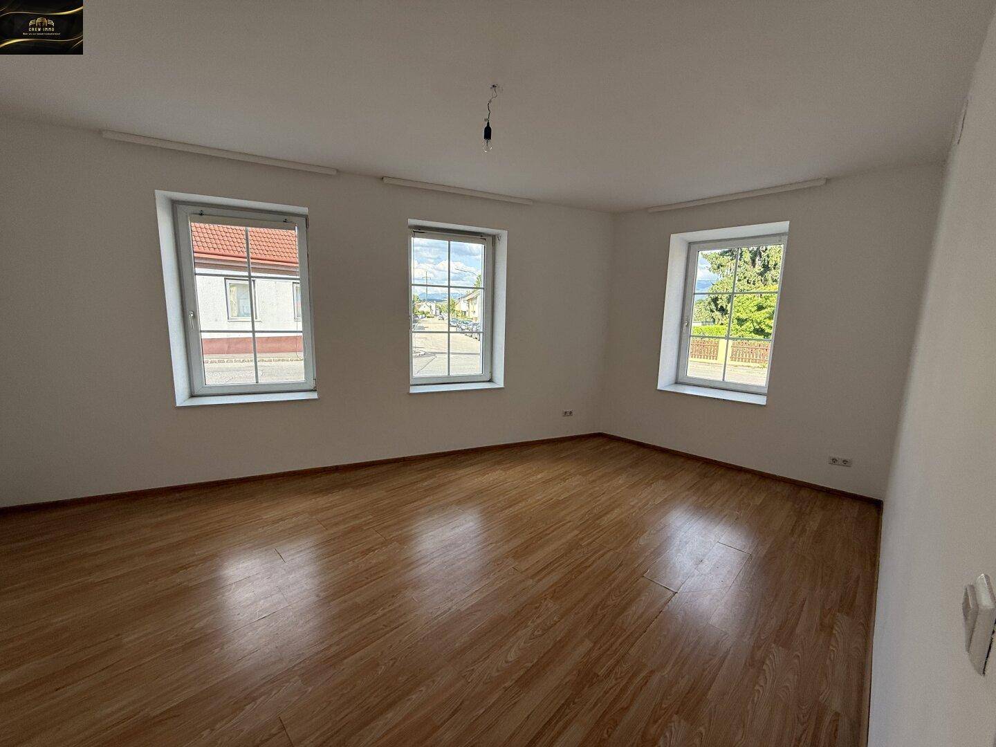 Heller Raum mit Laminatboden und drei Fenstern, die viel Tageslicht hereinlassen.