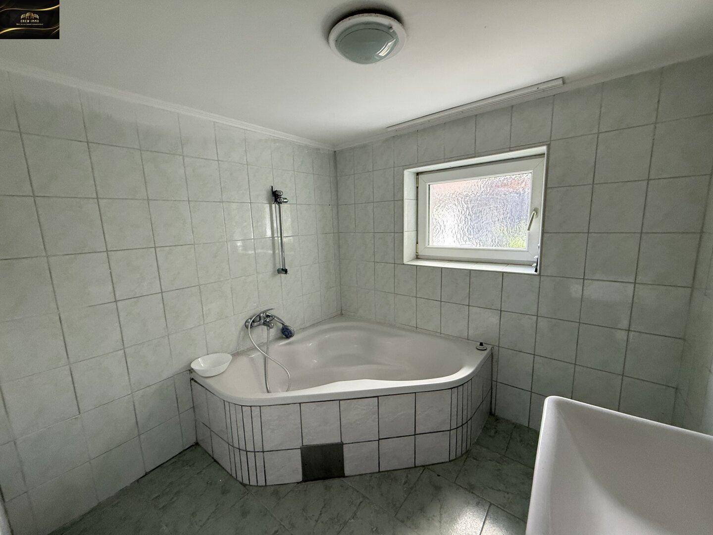 Gefliestes Badezimmer mit Eckbadewanne und einem kleinen Fenster für natürliche Belüftung.