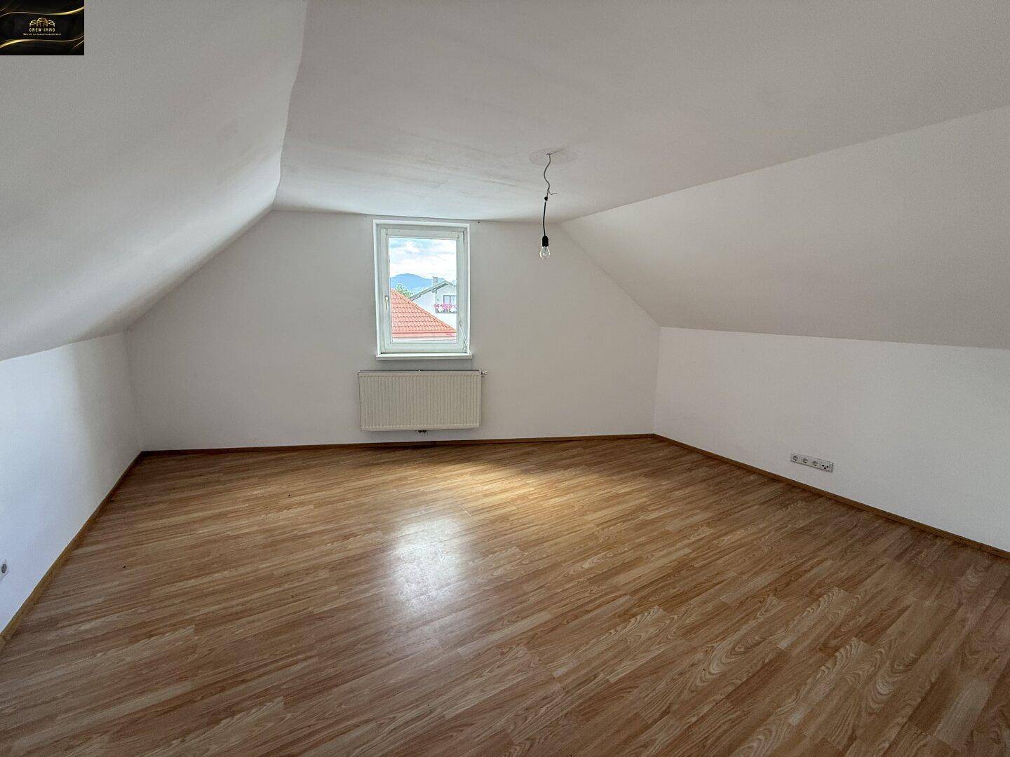Ausgebauter Dachbodenraum mit schrägen Wänden, Laminatboden und einem Fenster mit Bergblick.