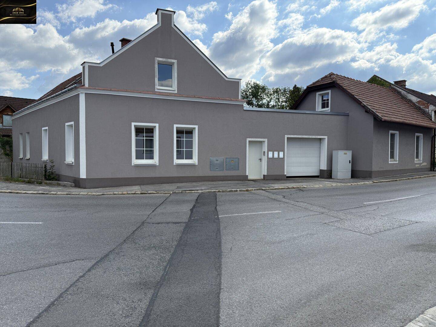 Graue Fassade eines Wohnhauses mit weißen Fenstern und einer integrierten Garage an der Straße.