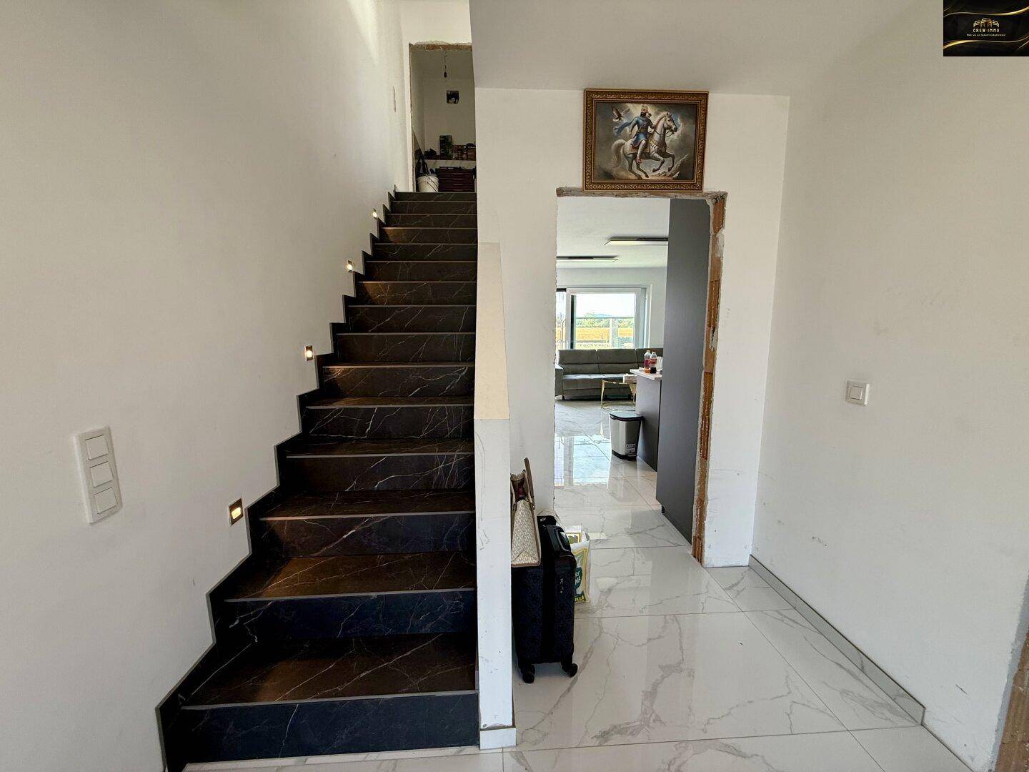 Elegante Treppe mit dunklen Marmorfliesen und integrierter Beleuchtung, die zum Wohnbereich führt.