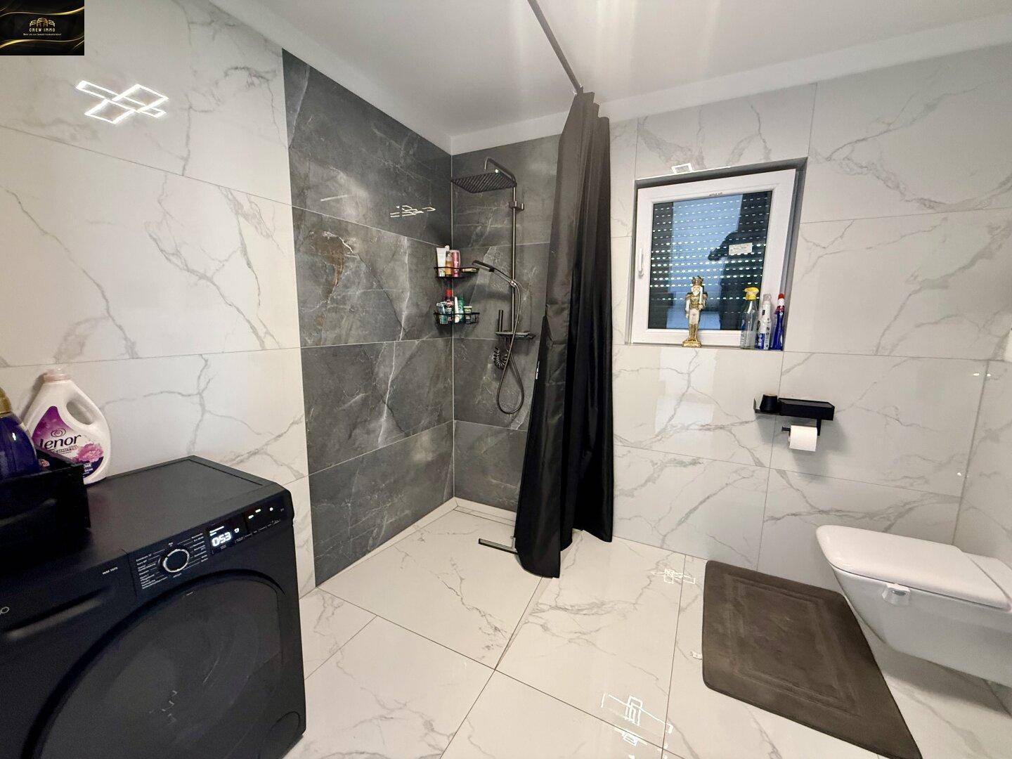 Modernes Badezimmer mit großer Dusche, Waschmaschine und hellen Marmorfliesen.