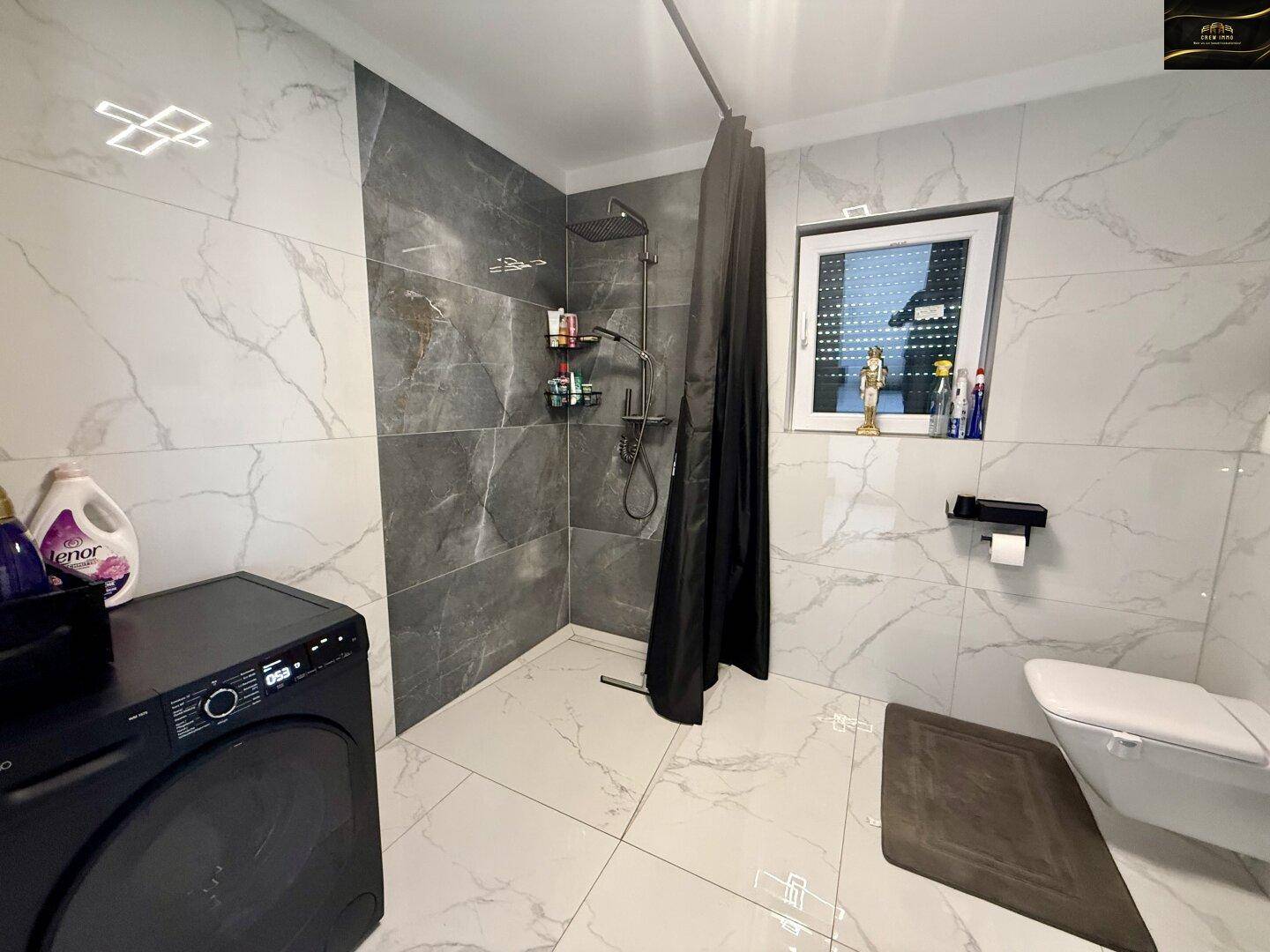 Modernes Badezimmer mit großformatigen Fliesen, ebenerdiger Dusche und wandhängendem WC.