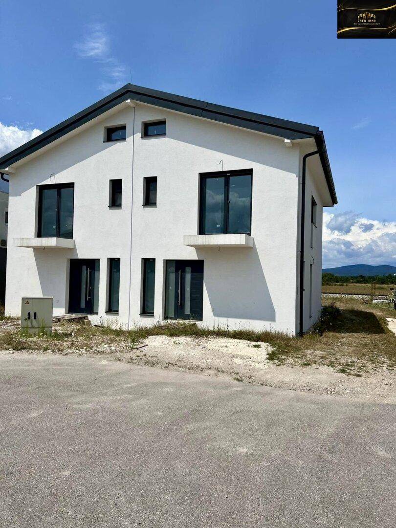 Modernes Einfamilienhaus mit weißer Fassade, dunklen Fenstern und klaren architektonischen Linien.