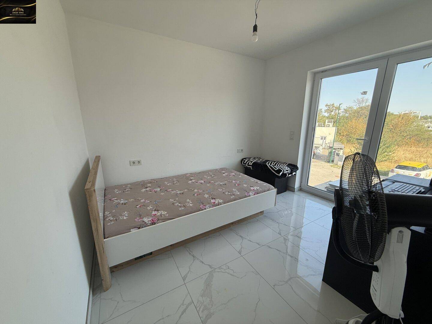 Helles Schlafzimmer mit Einzelbett, Fliesenboden und Zugang zum Außenbereich.