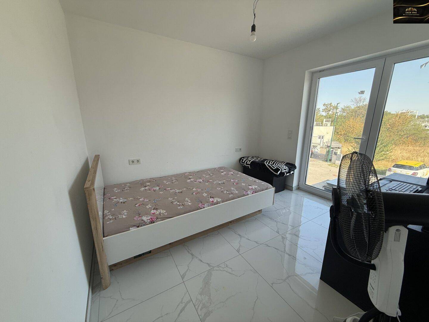 Freundliches Schlafzimmer mit Einzelbett, hellen Fliesen und großem Fenster für viel Tageslicht.