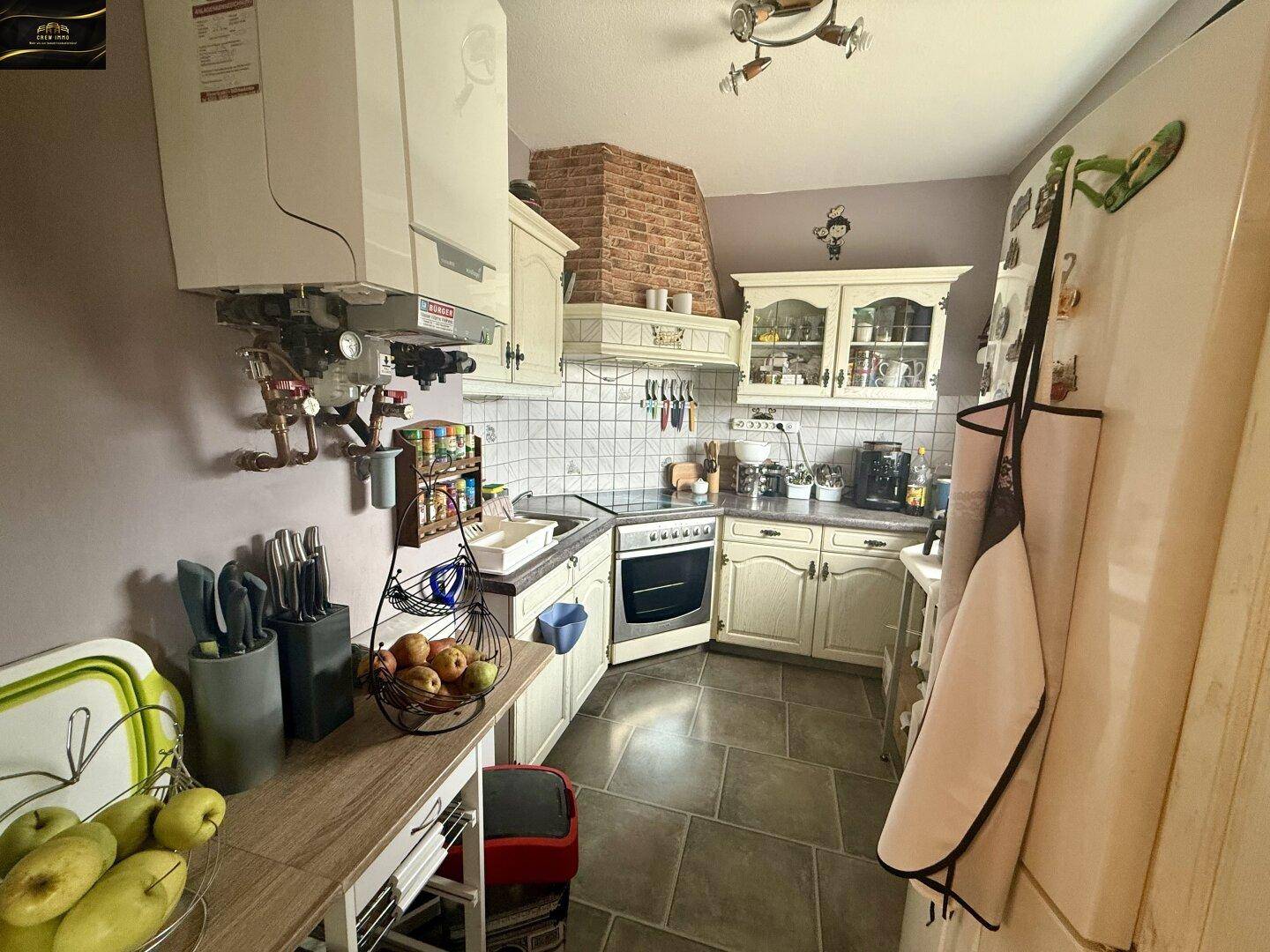 Funktionale Küche mit hellen Schränken, Fliesenboden und Backofen, inklusive Wandheizkessel.