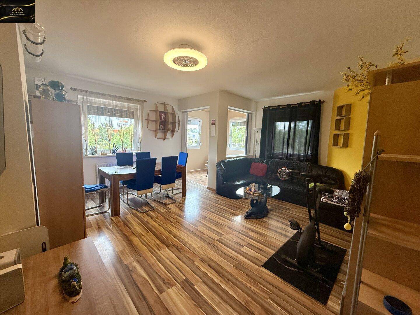 Geräumiger Wohn-Essbereich mit Holzboden, schwarzem Sofa und Esstisch mit blauen Stühlen.