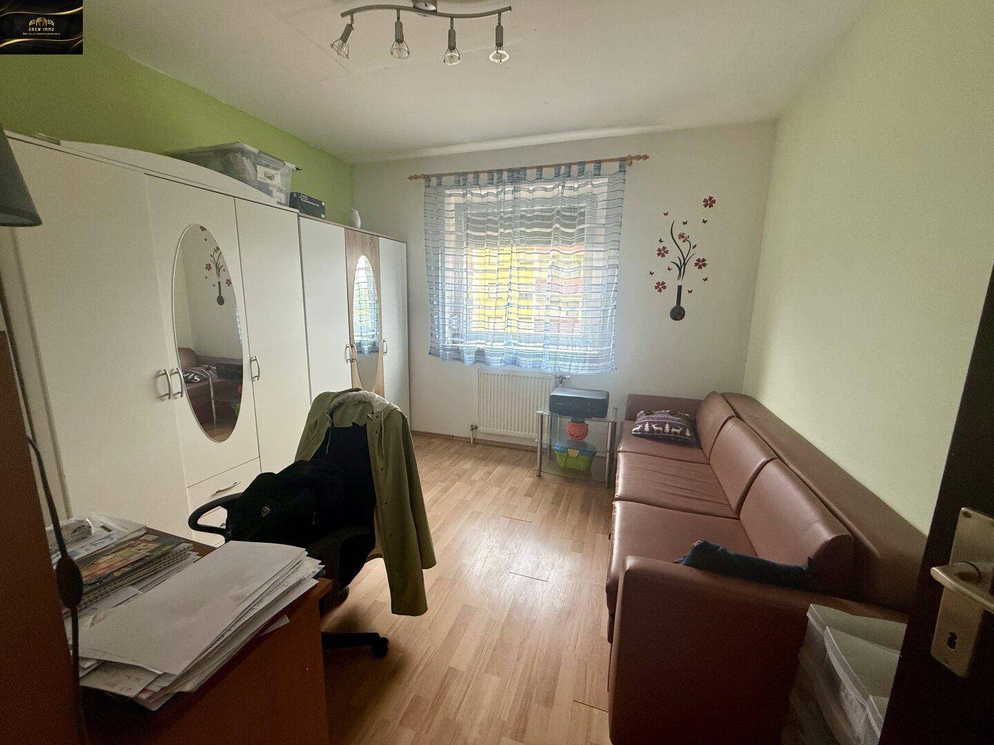 Helles Schlafzimmer mit grün gestrichenen Wänden, braunem Sofa und großem Kleiderschrank.