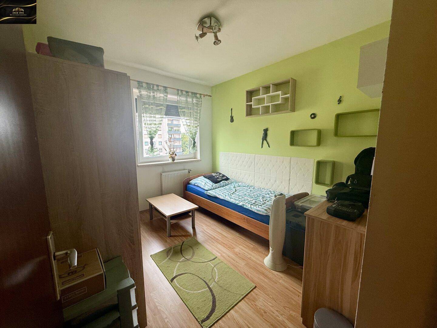 Freundliches Schlafzimmer mit Einzelbett, grün gestrichenen Wänden und Holzboden.