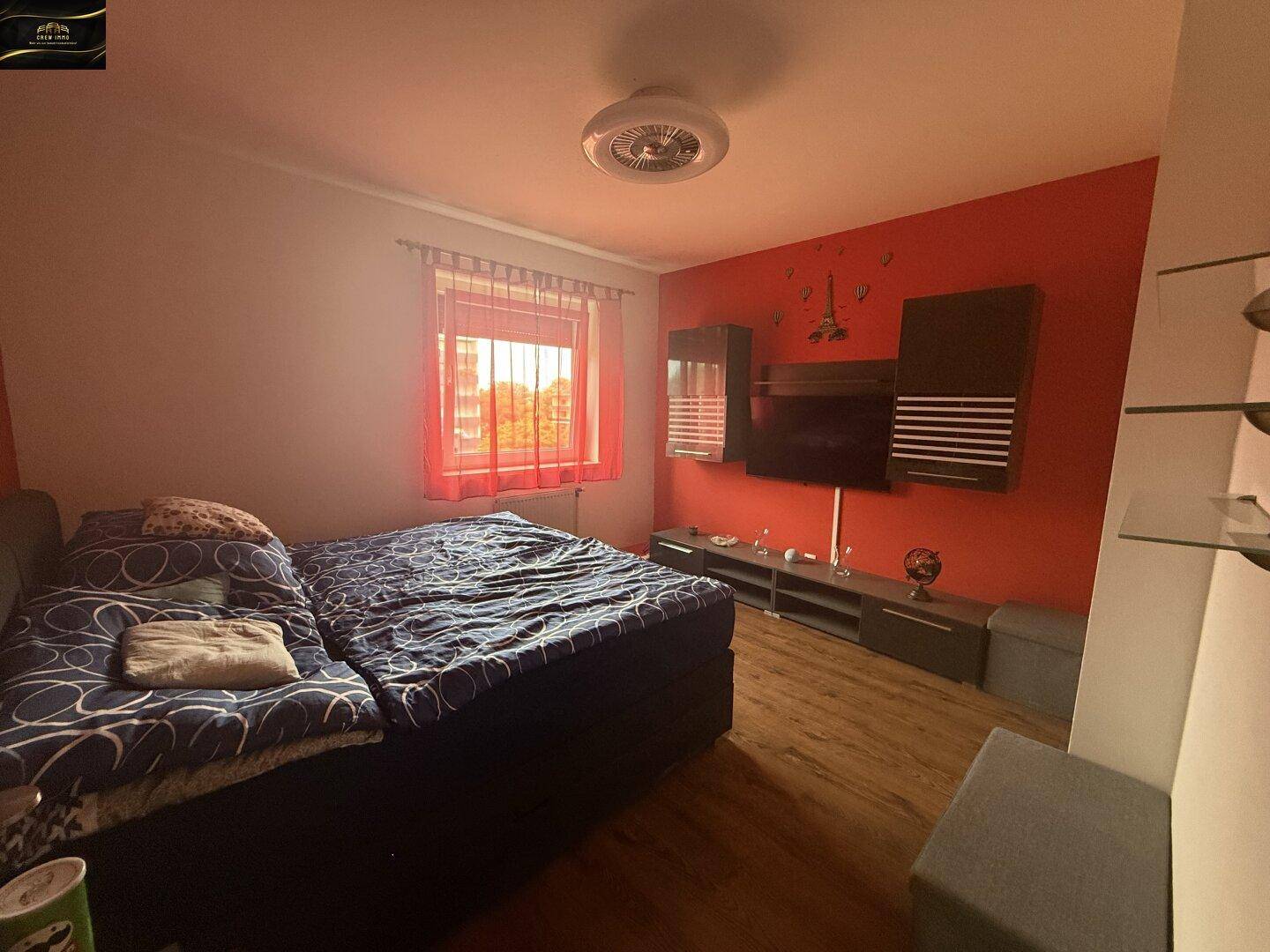 Schlafzimmer mit großem Bett, roter Akzentwand und an der Wand montiertem Fernseher.