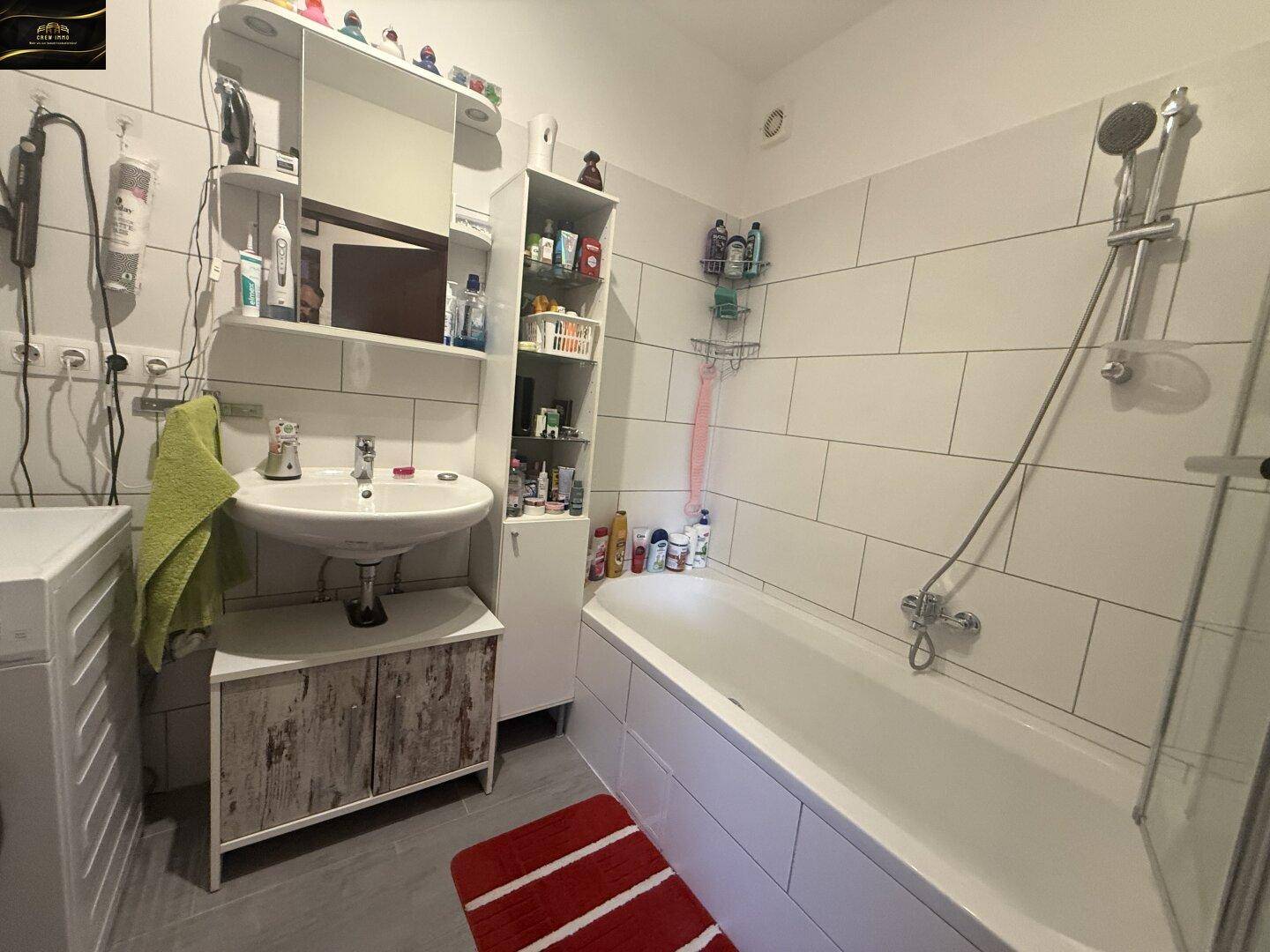 Modernes Badezimmer mit Badewanne, Dusche, Waschbecken und Waschmaschine, hell gefliest.