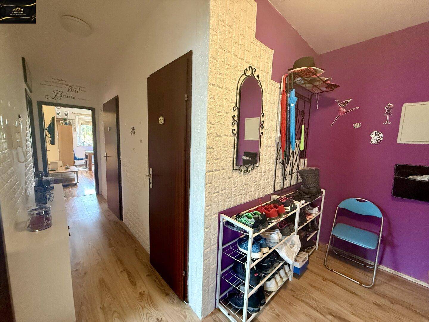 Heller Flur mit Schuhregal, Garderobe, Spiegel und einer auffälligen lila Akzentwand.