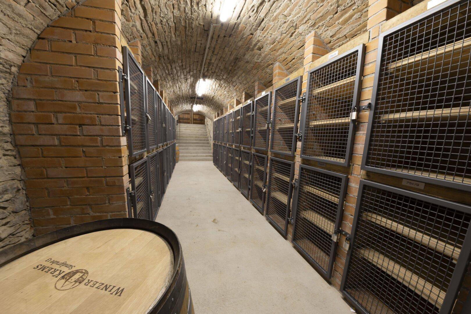 Historischer Kellerraum mit Ziegelwänden, Gewölbedecke und abschließbaren Lagerabteilen sowie einem Weinfass.