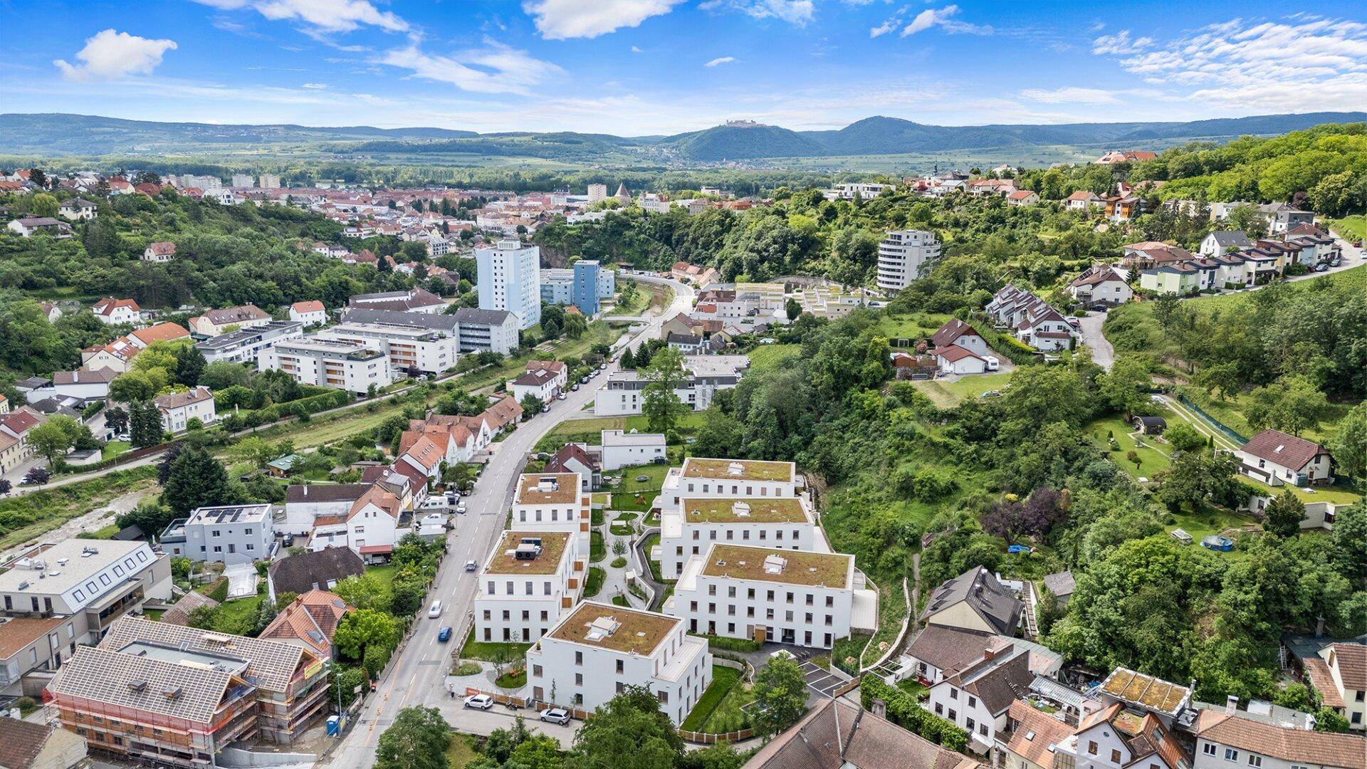 Luftaufnahme der modernen Wohnanlage, eingebettet in eine grüne Hügellandschaft mit Blick auf die Stadt.