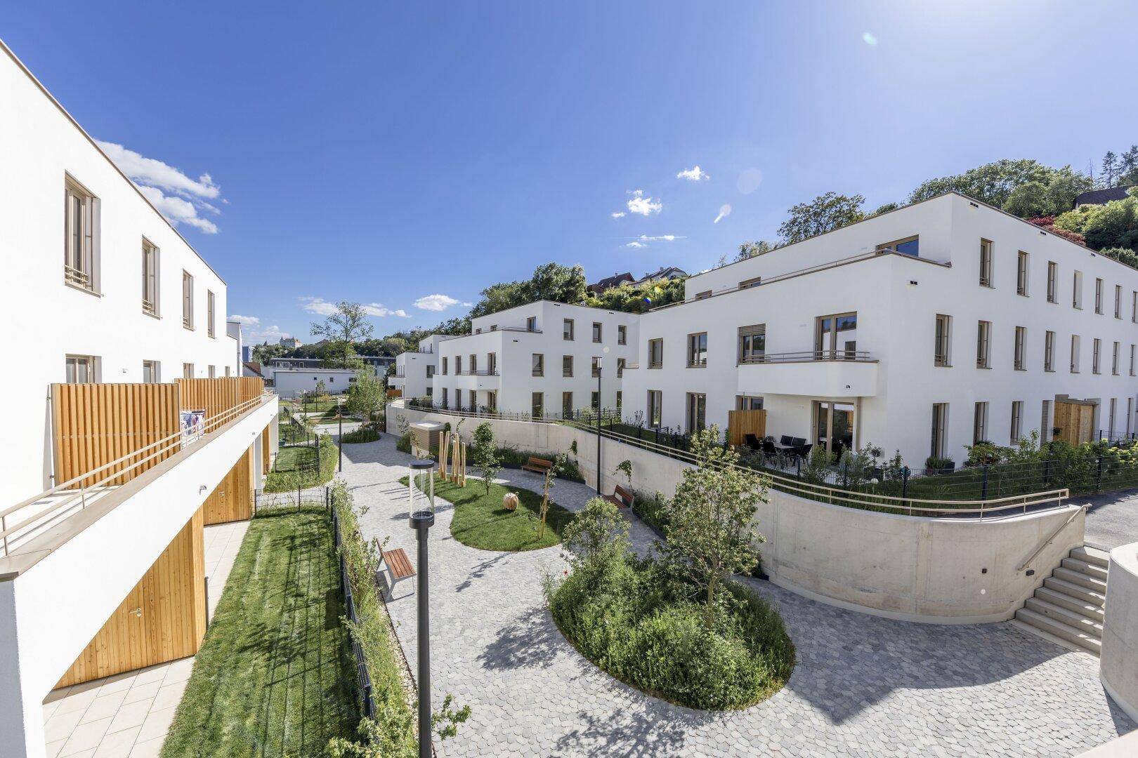 Panoramablick auf eine moderne Wohnsiedlung mit weißen Fassaden und terrassierten Grünanlagen.