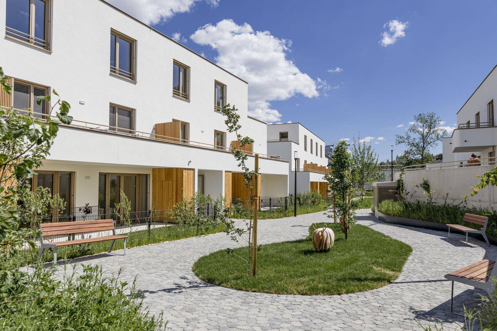 Moderne Wohngebäude mit weißer Fassade und begrüntem Innenhof mit Gehwegen und Bänken.