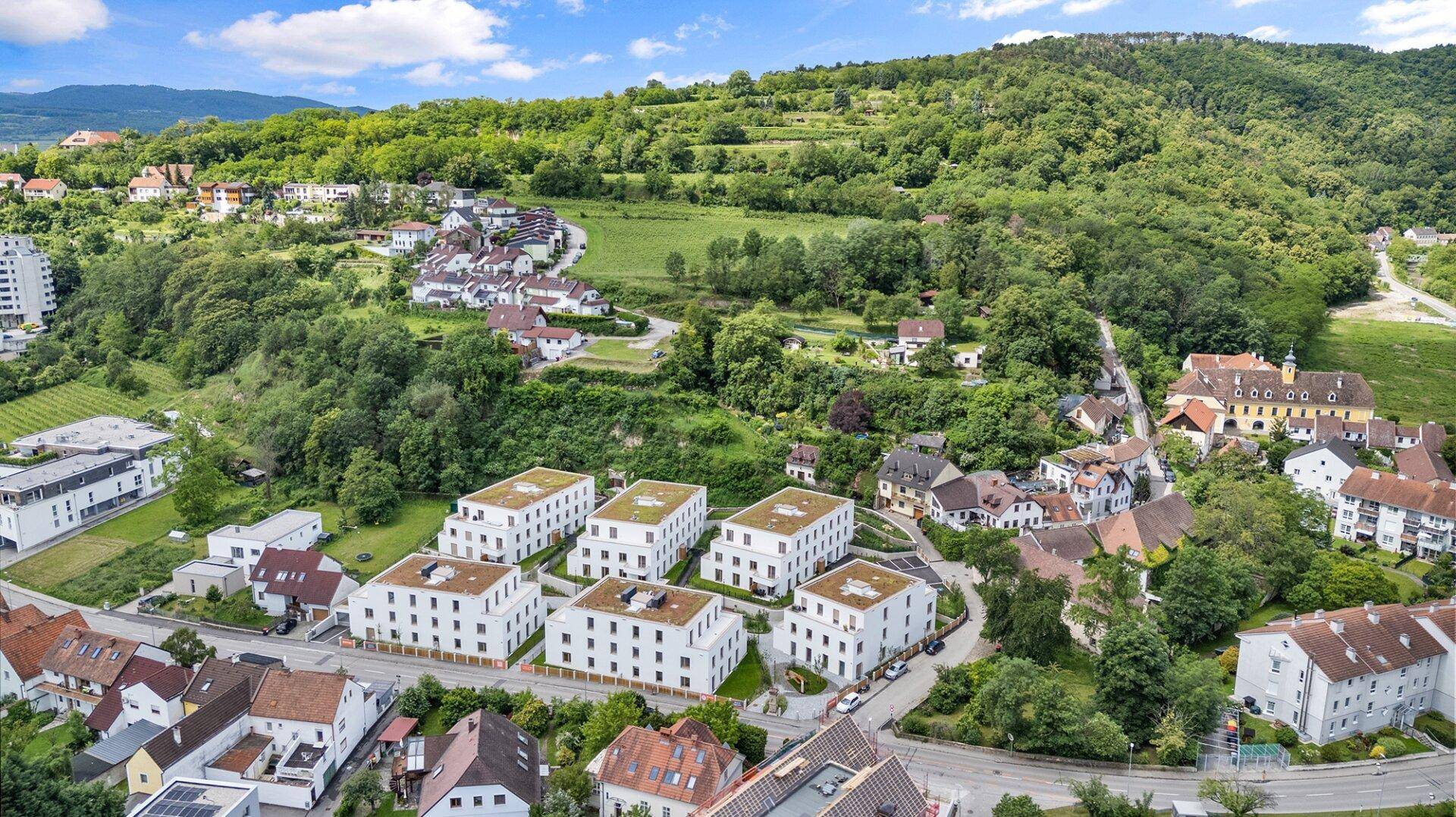 Luftaufnahme einer modernen Wohnsiedlung eingebettet in eine grüne Hügellandschaft mit Weinbergen.