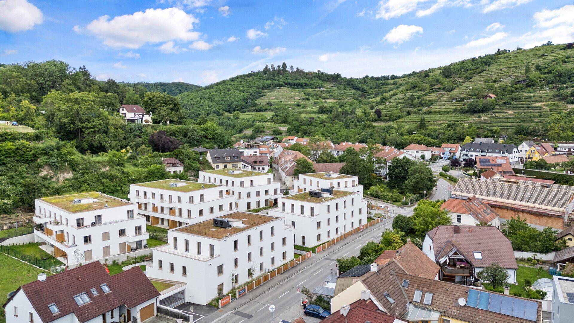 Luftaufnahme einer modernen Wohnsiedlung mit Flachdächern und umliegender grüner Landschaft.