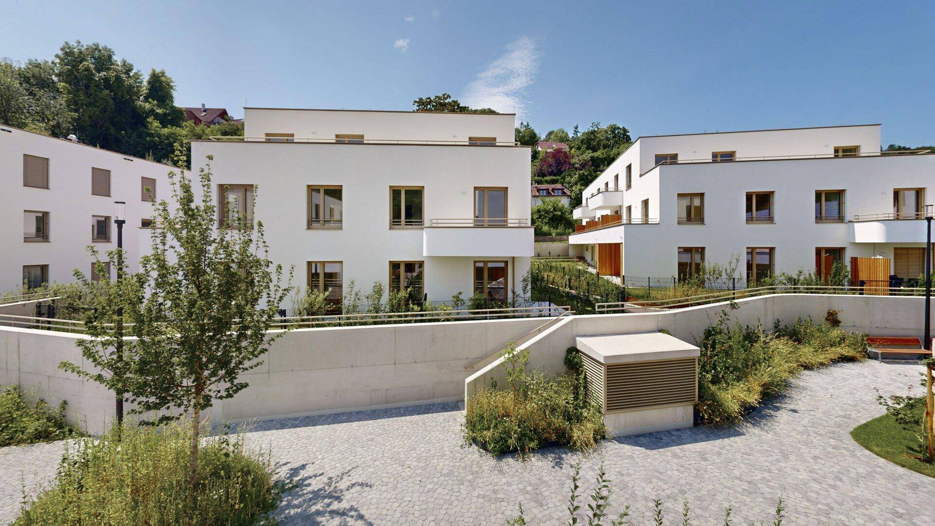 Moderne Wohnanlage mit weißer Fassade und begrüntem Innenhof unter blauem Himmel.
