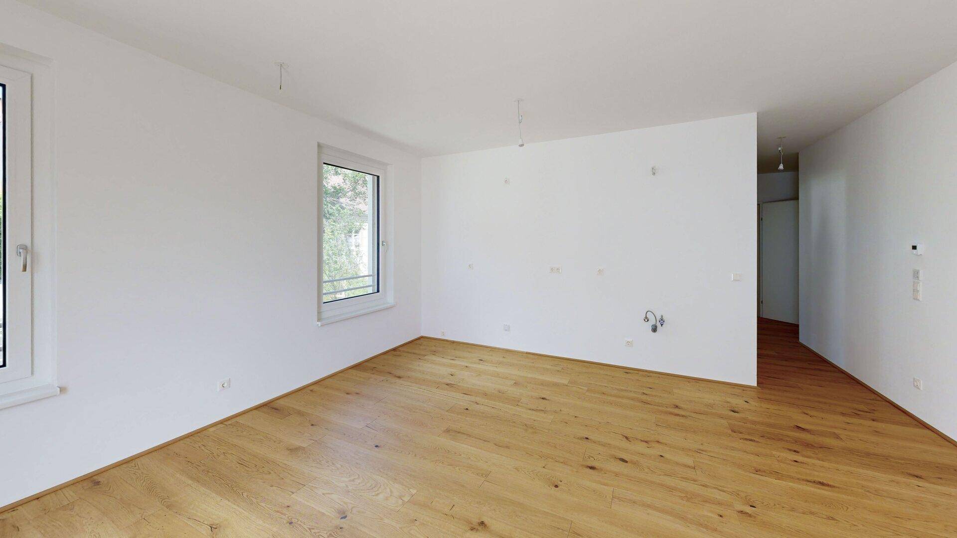 Geräumiger, heller Wohnbereich mit Holzboden und großen Fenstern, bereit zur Einrichtung.