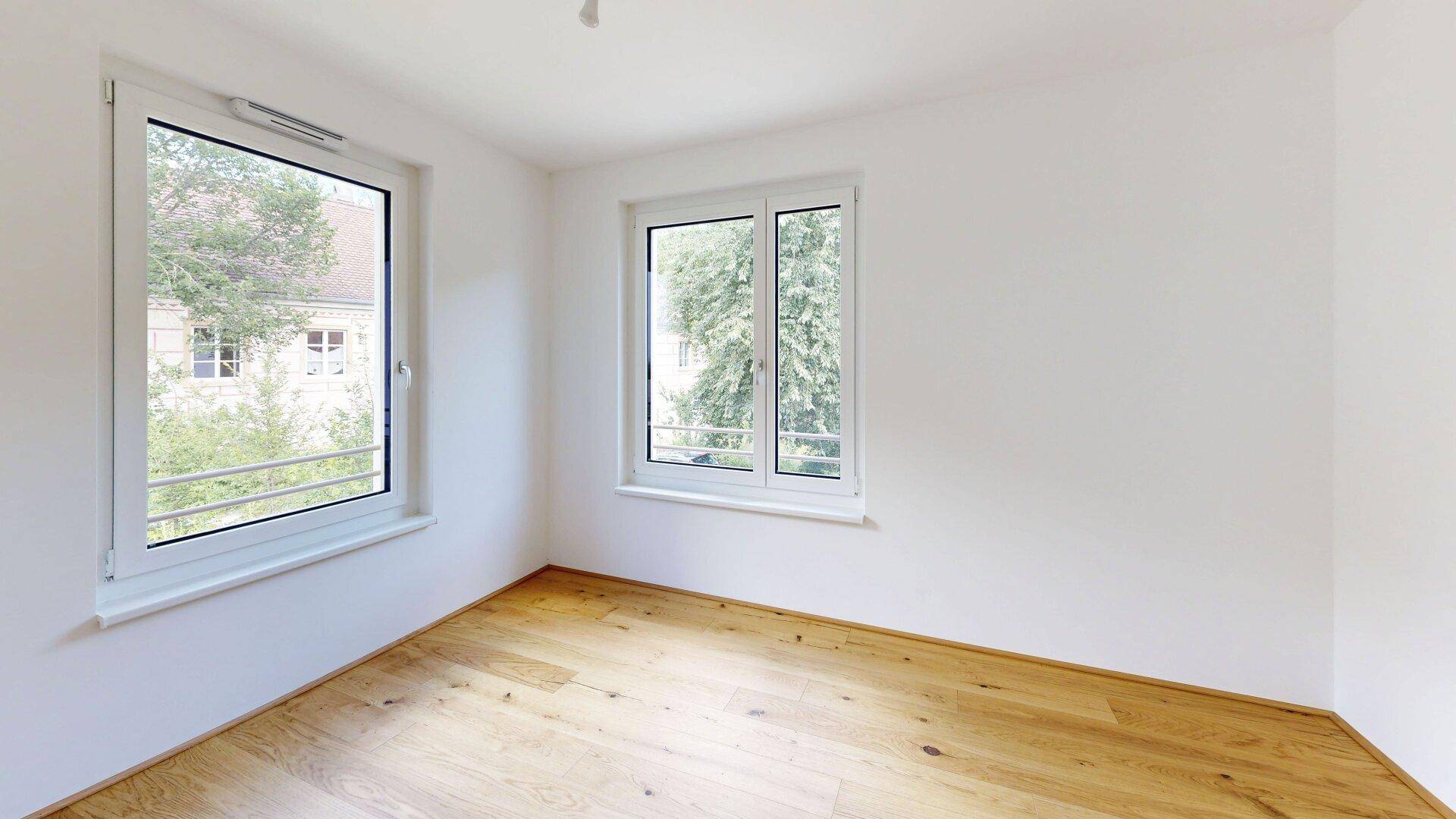 Helles Schlafzimmer mit Holzboden und zwei Fenstern, bietet viel Tageslicht und Ausblick.