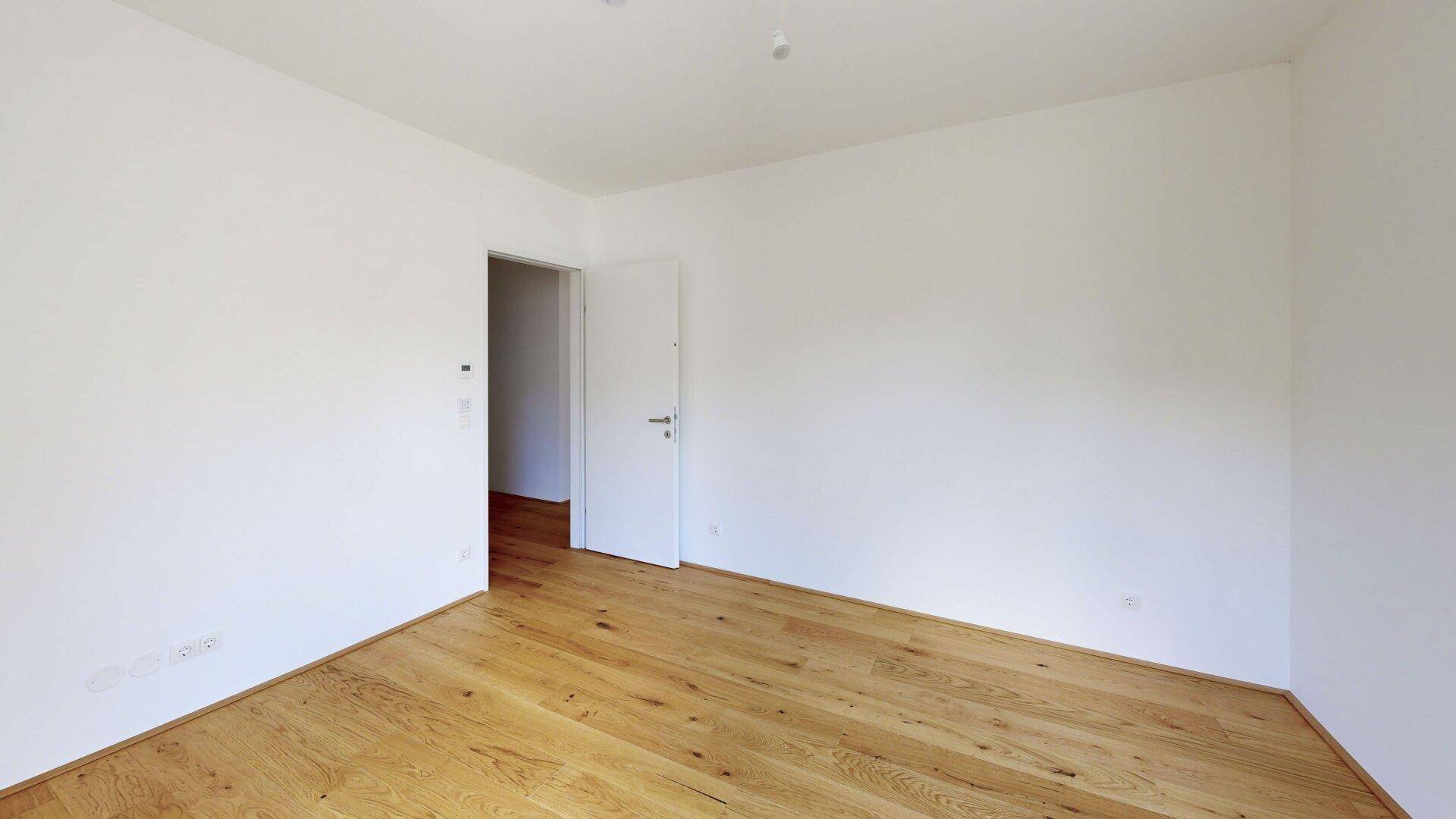 Ruhiges Schlafzimmer mit Holzboden und weiß gestrichenen Wänden, bereit zur individuellen Gestaltung.