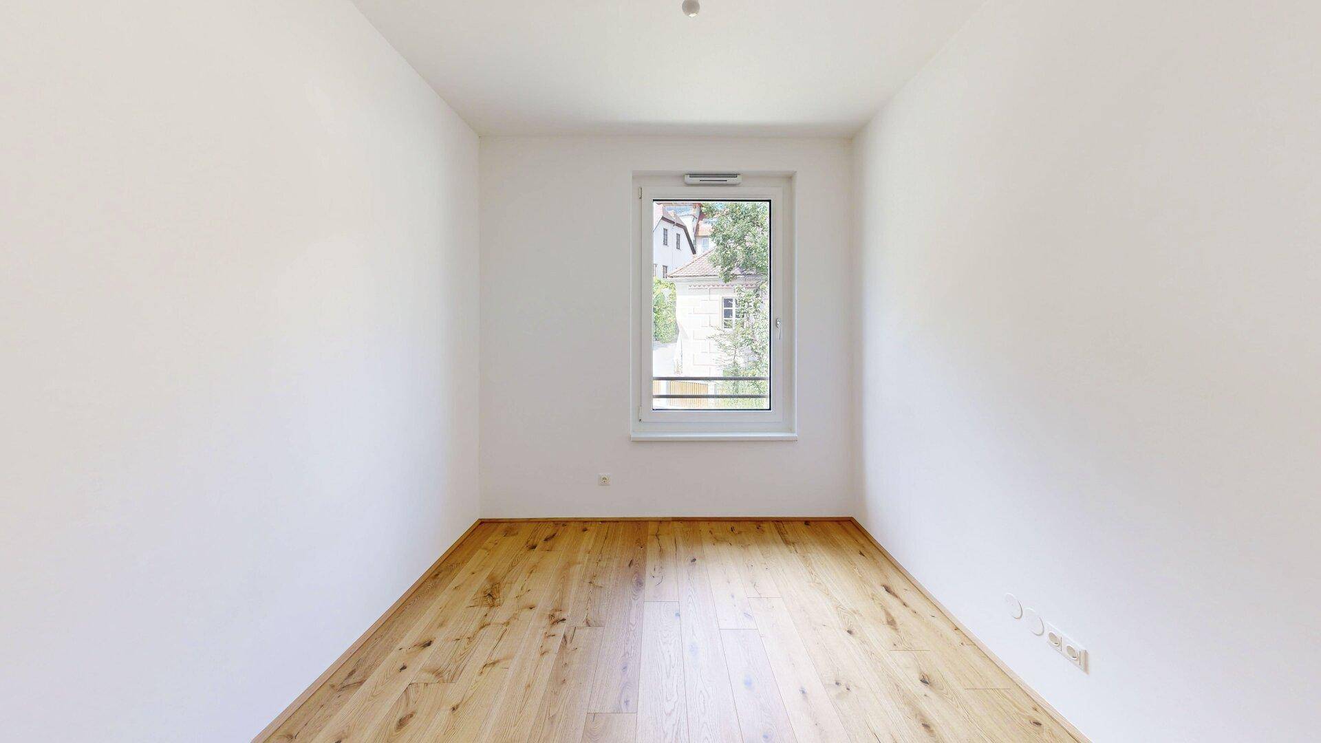 Kompaktes Schlafzimmer mit Holzboden und einem Fenster, ideal als Kinder- oder Arbeitszimmer.