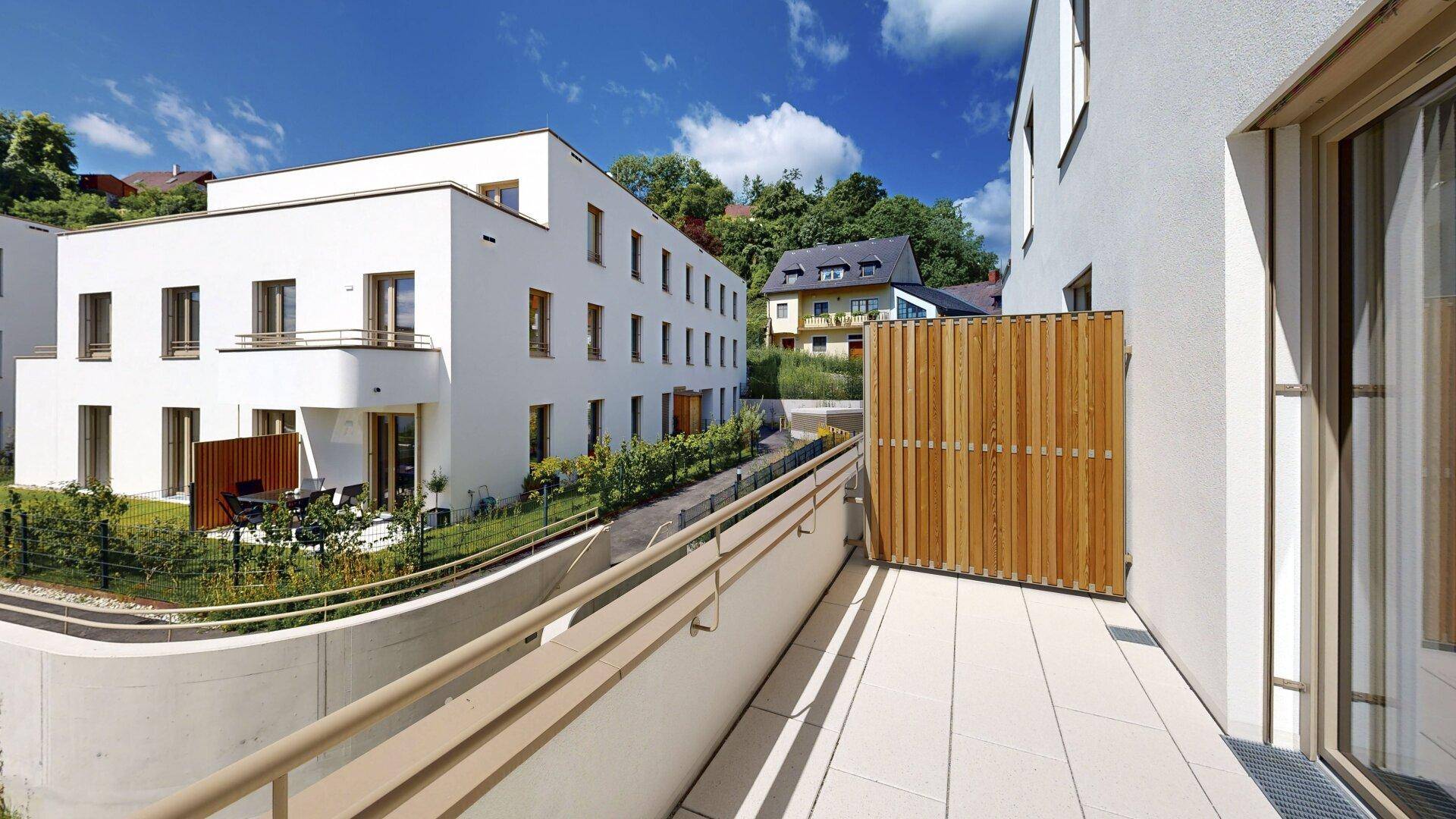 Blick vom Balkon auf die moderne Wohnanlage mit gepflegten Grünflächen und weiteren Gebäuden.