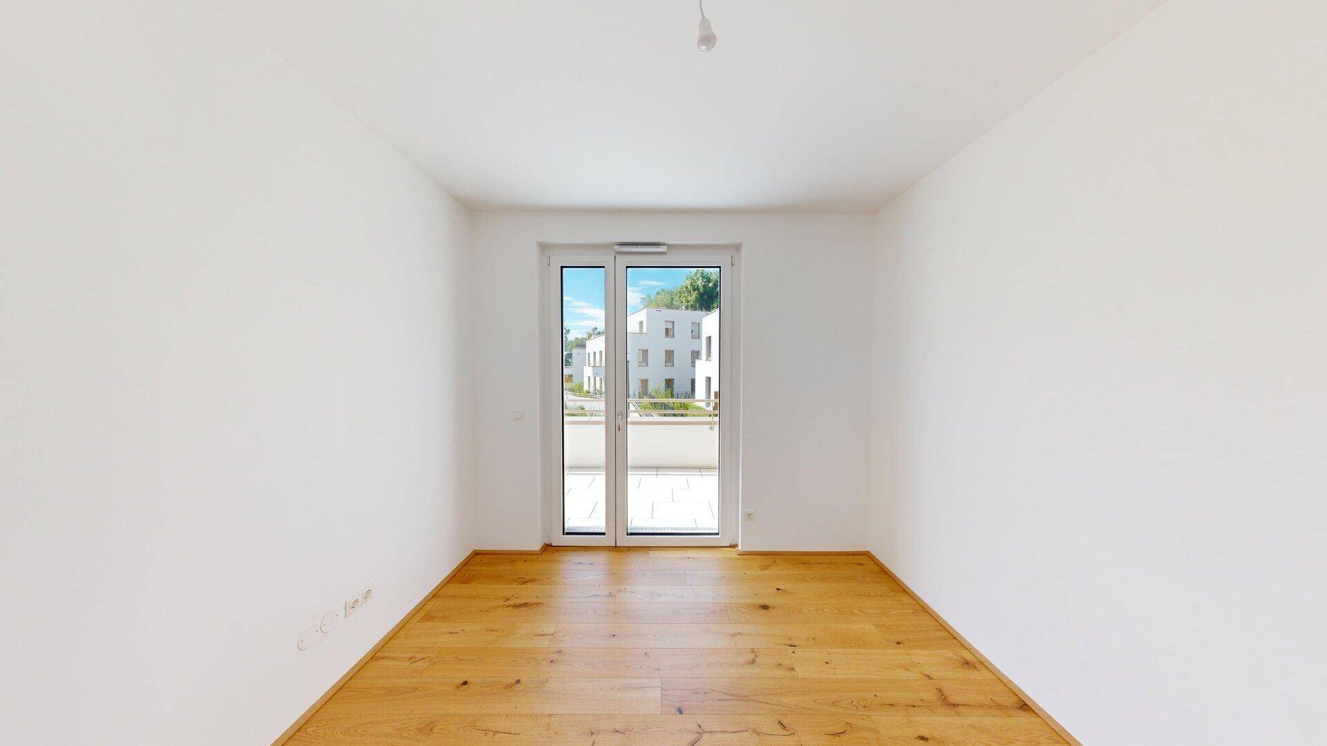 Helles Schlafzimmer mit Parkettboden, weißen Wänden und direktem Zugang zu einem Balkon.