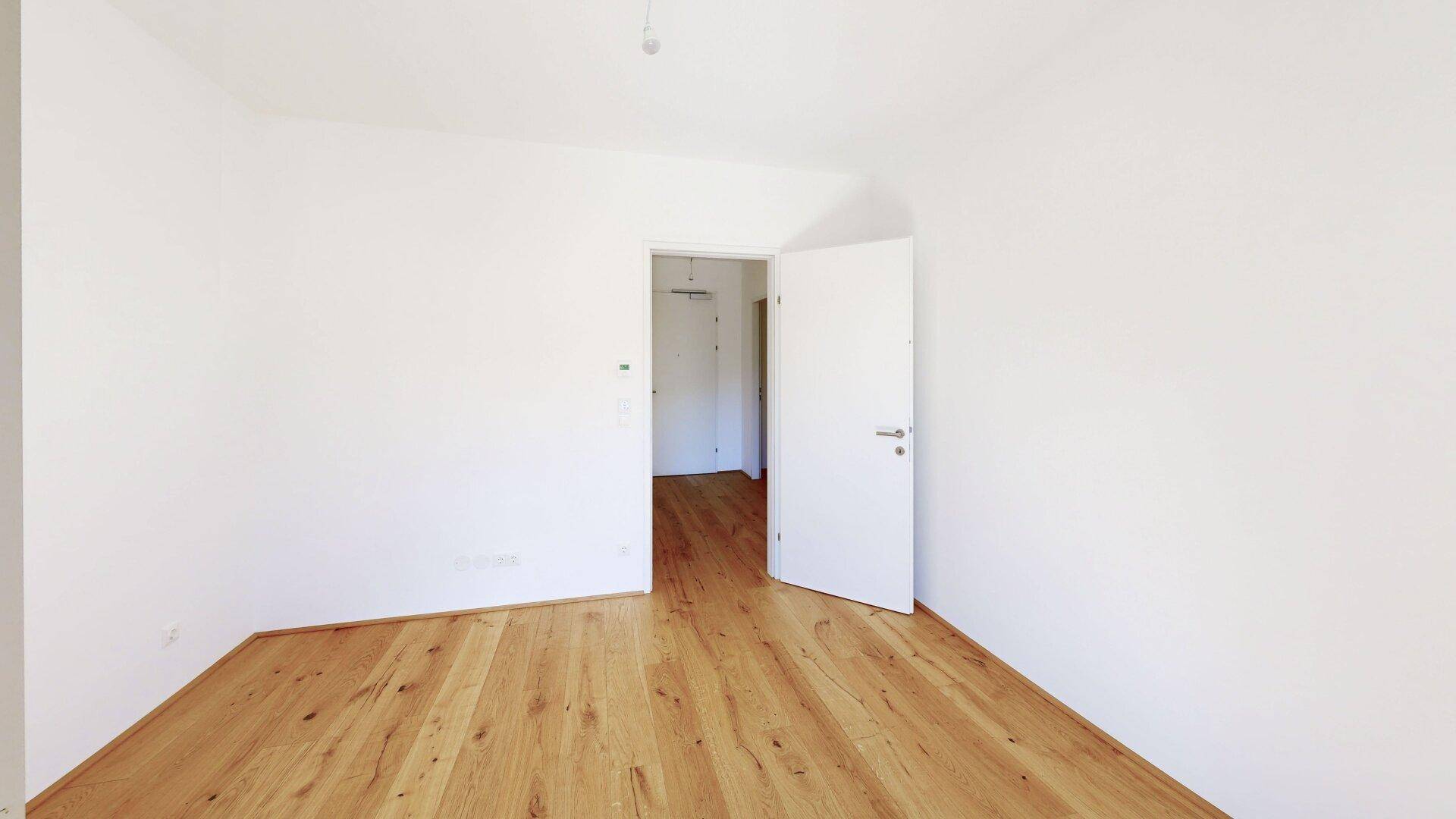 Leeres Zimmer mit Parkettboden und weiß gestrichenen Wänden, bereit zur individuellen Gestaltung.