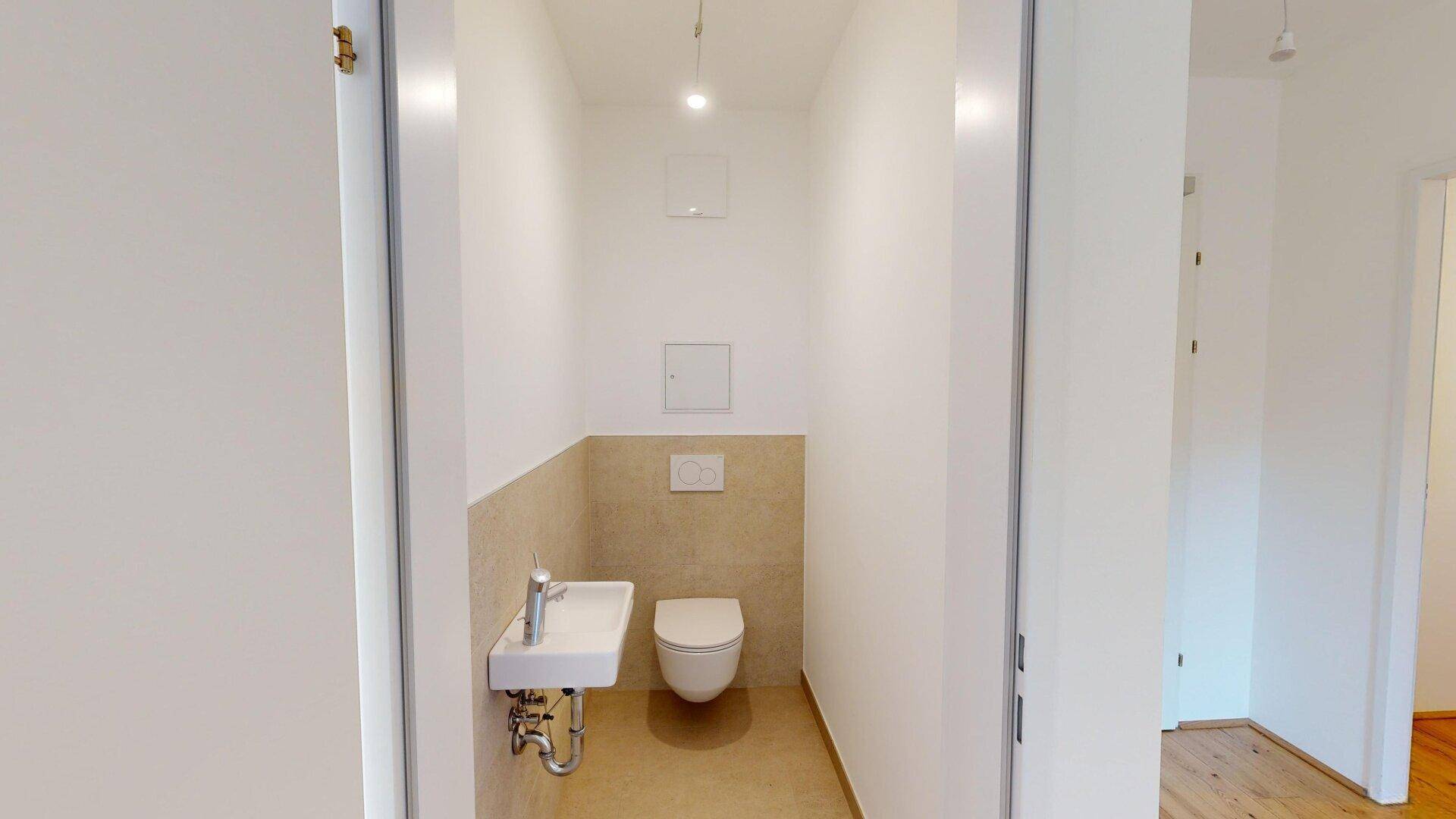 Gäste-WC mit wandhängender Toilette, kleinem Waschbecken und hellen Fliesen im unteren Bereich.