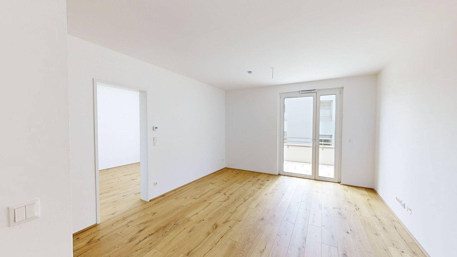 Helles, leeres Zimmer mit Holzboden und Zugang zu einem Balkon, bereit zur individuellen Gestaltung.