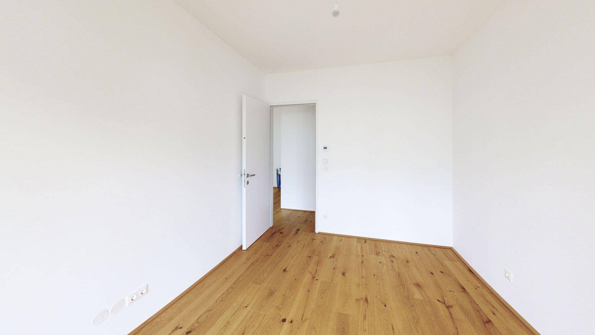 Leeres Zimmer mit Holzboden und offener Tür, bereit für individuelle Gestaltung.