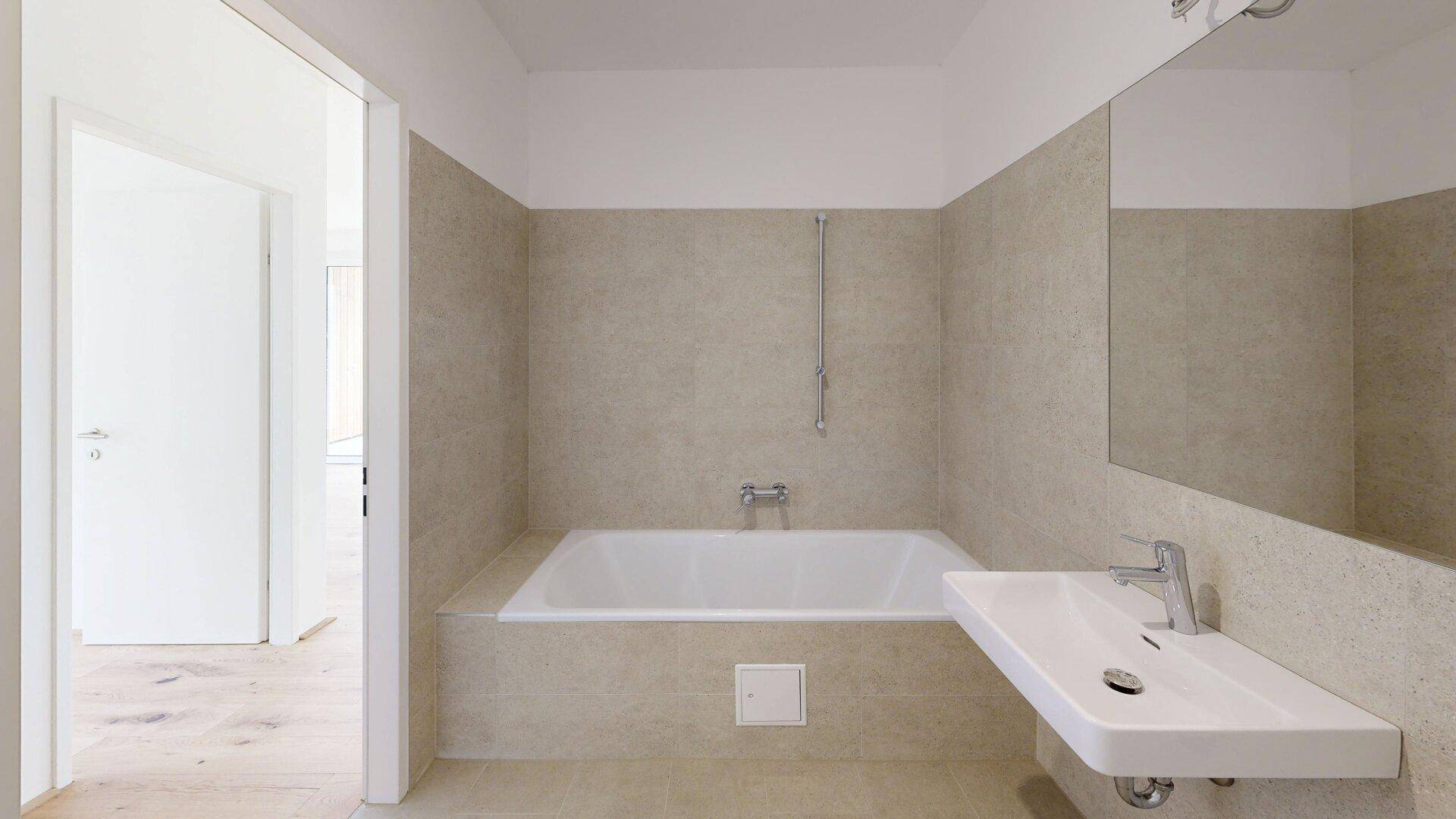 Modernes Badezimmer mit Badewanne, Waschbecken und hellen Fliesen an den Wänden.