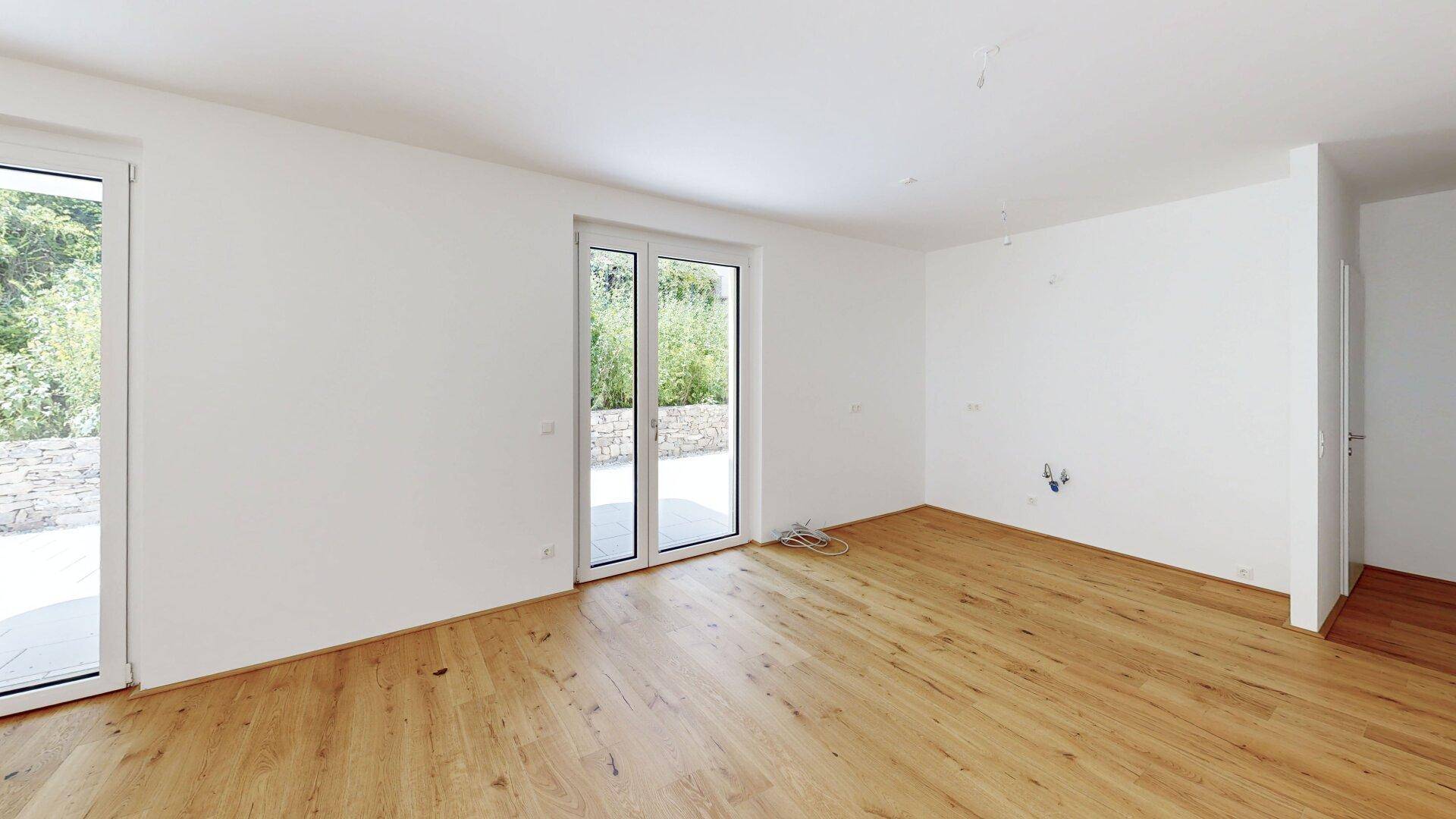 Geräumiges, unmöbliertes Zimmer mit hellem Holzboden und Zugang zu einem Außenbereich.