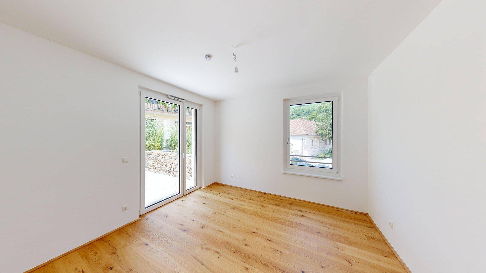Helles Schlafzimmer mit Holzboden und Zugang zu einem Außenbereich sowie einem Fenster.