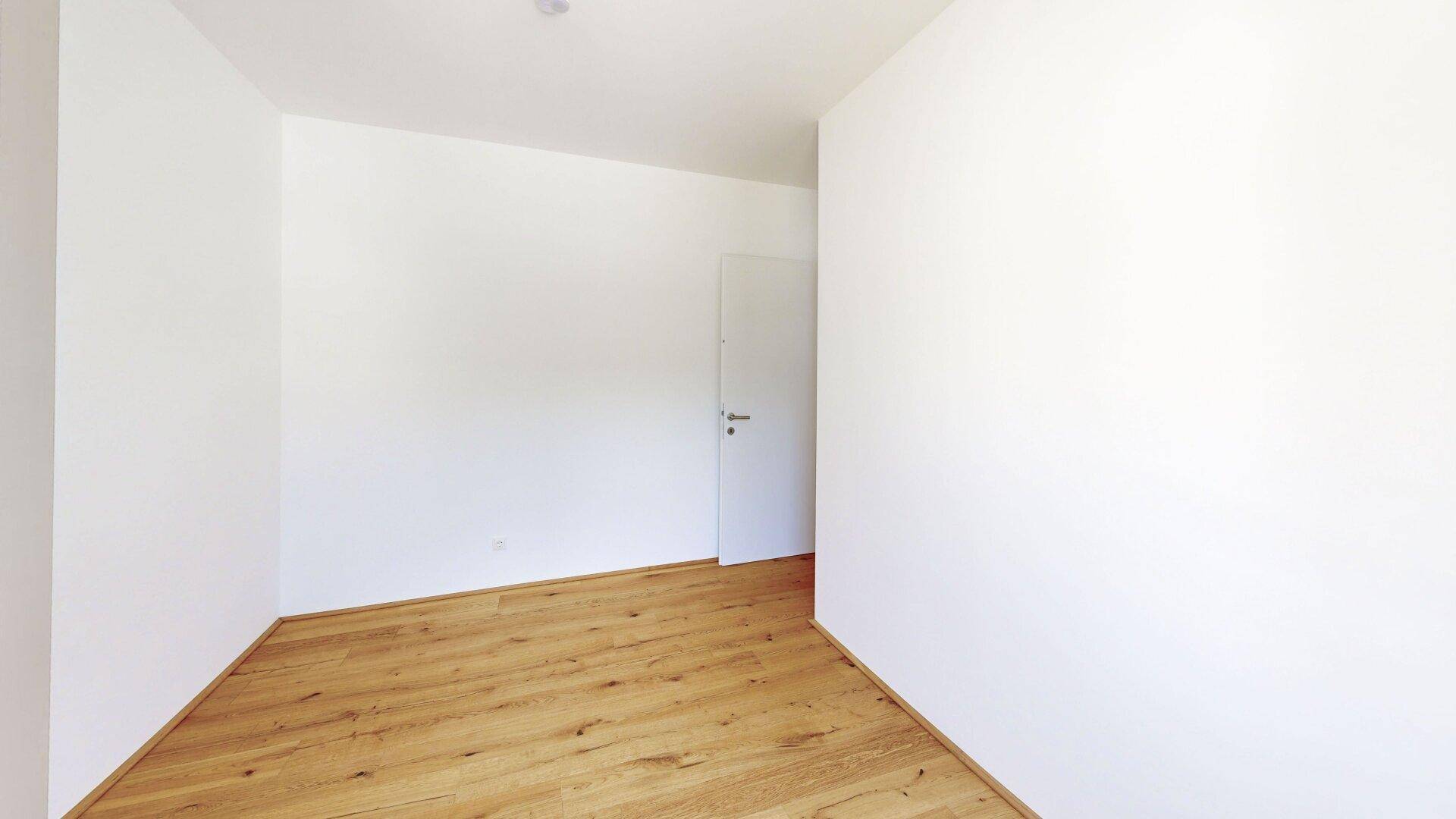 Leeres Zimmer mit hellem Holzboden und weiß gestrichenen Wänden, bereit zur Einrichtung.