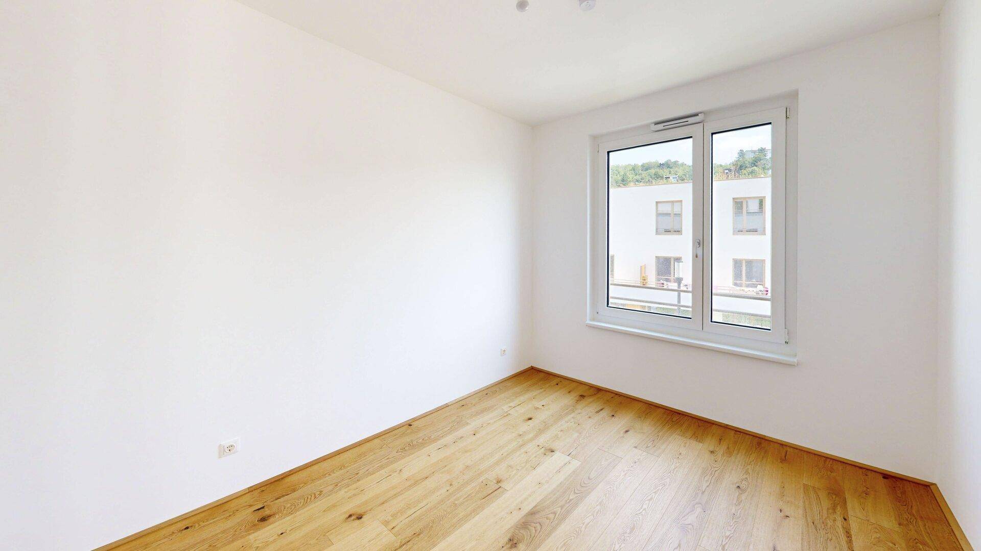 Helles Schlafzimmer mit Parkettboden und einem Fenster, das den Blick auf die Umgebung freigibt.
