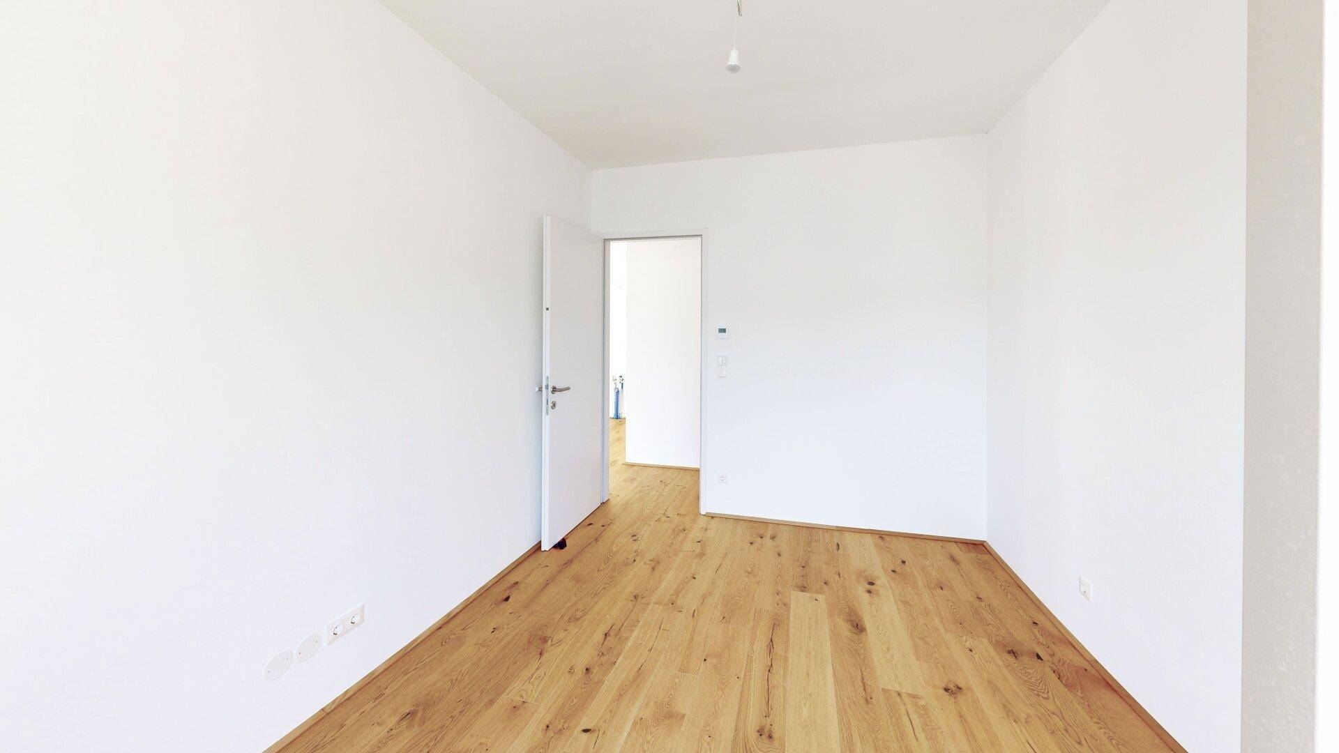 Heller Flur mit Holzboden und weiß gestrichenen Wänden, der zu weiteren Räumen führt.