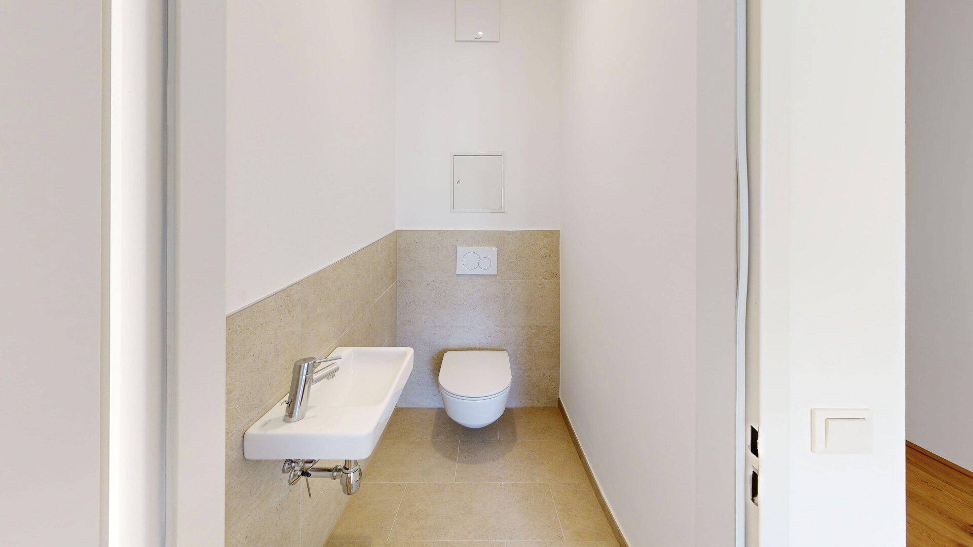 Kleines Gäste-WC mit wandhängender Toilette, kleinem Waschbecken und hellen Fliesen.